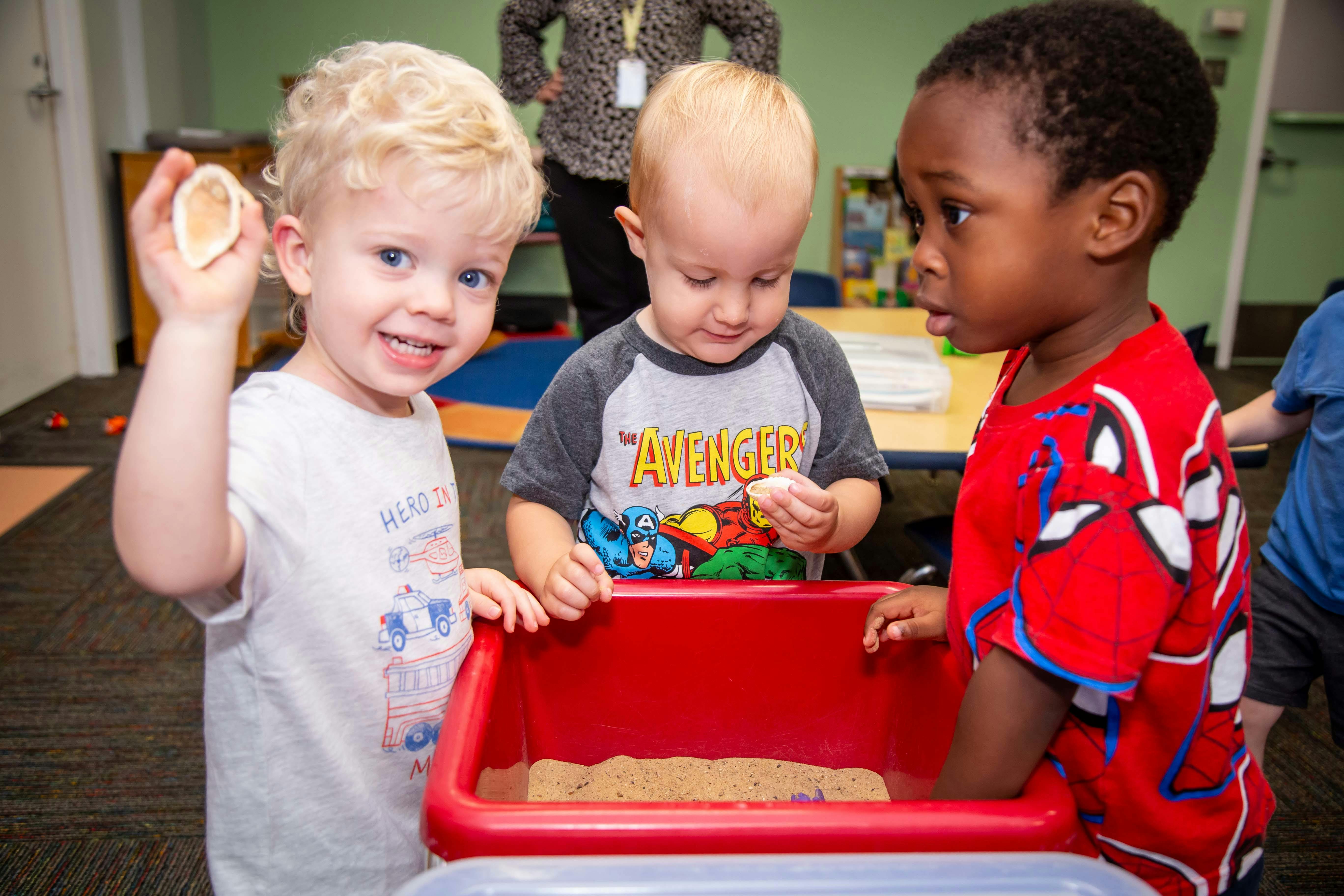 Three children playing with sand in a red bin