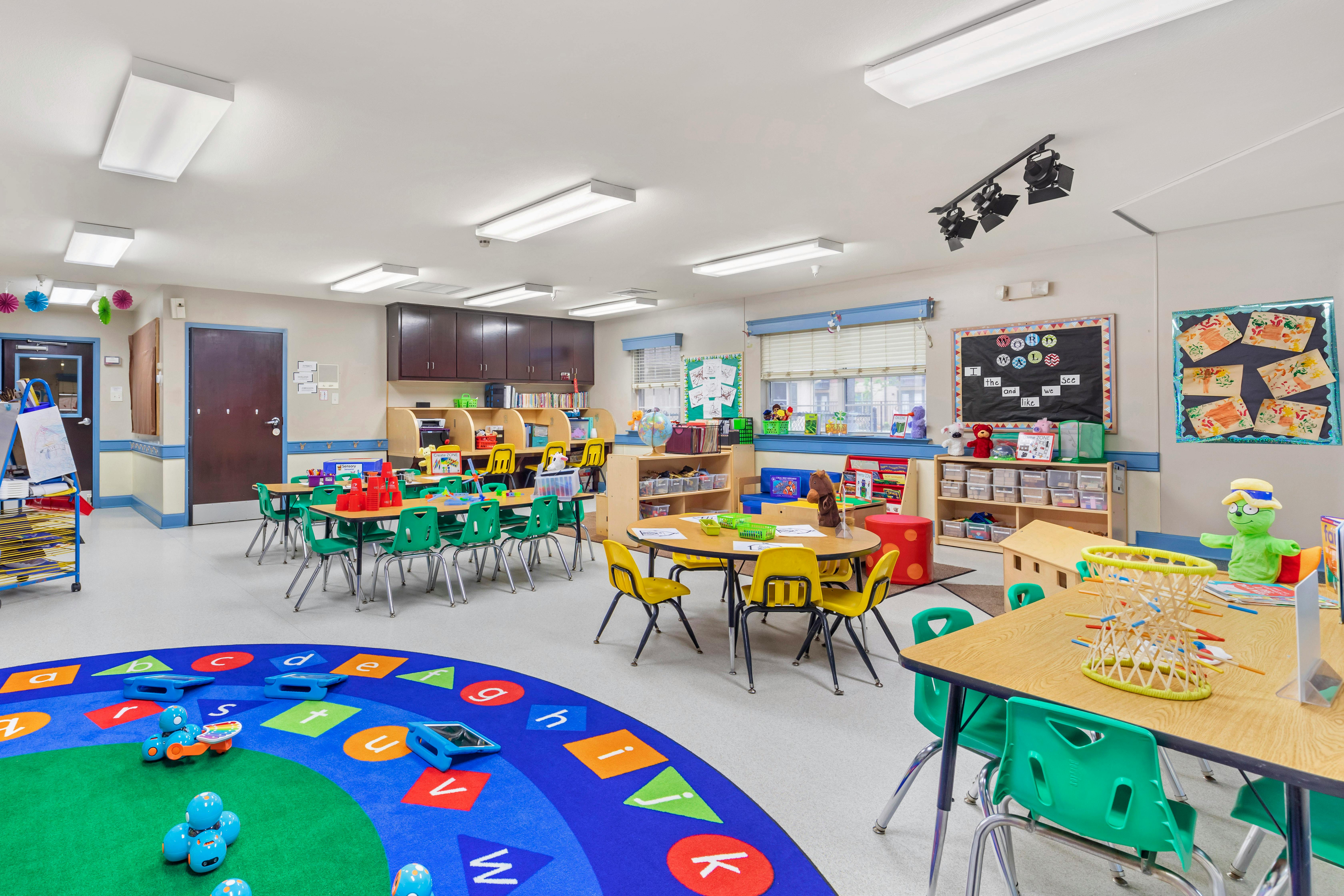 An empty early childhood classroom with colorful carpets, tables, chairs, and learning materials
