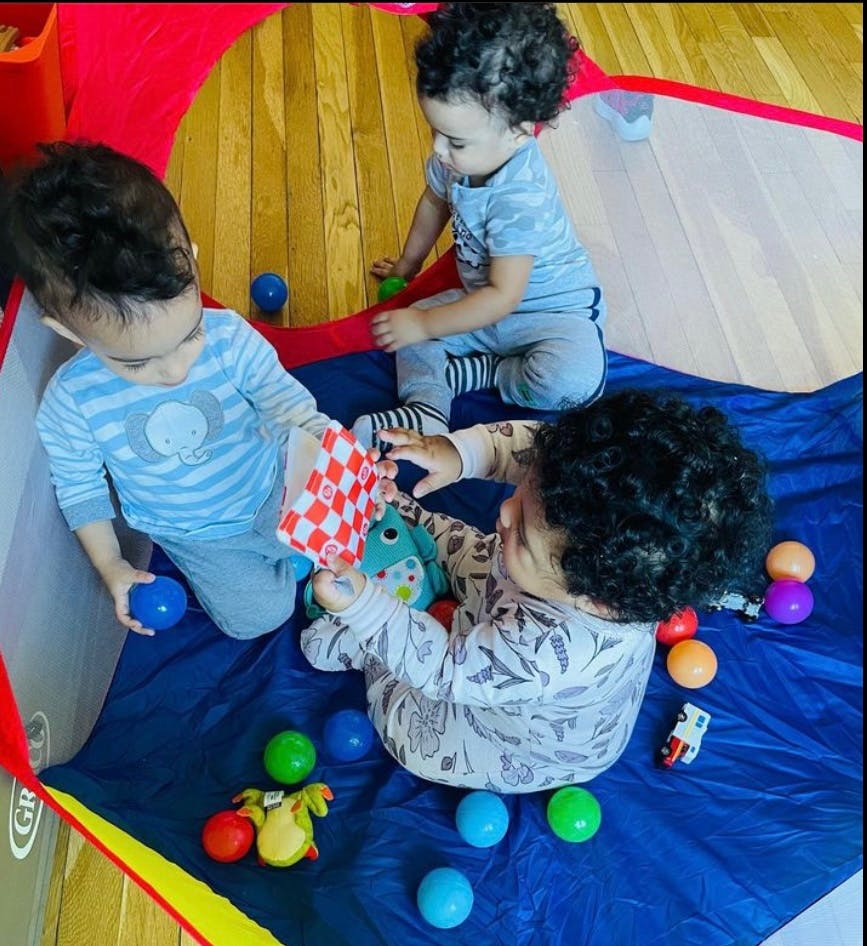Three children playing with balls and toys in a playpen