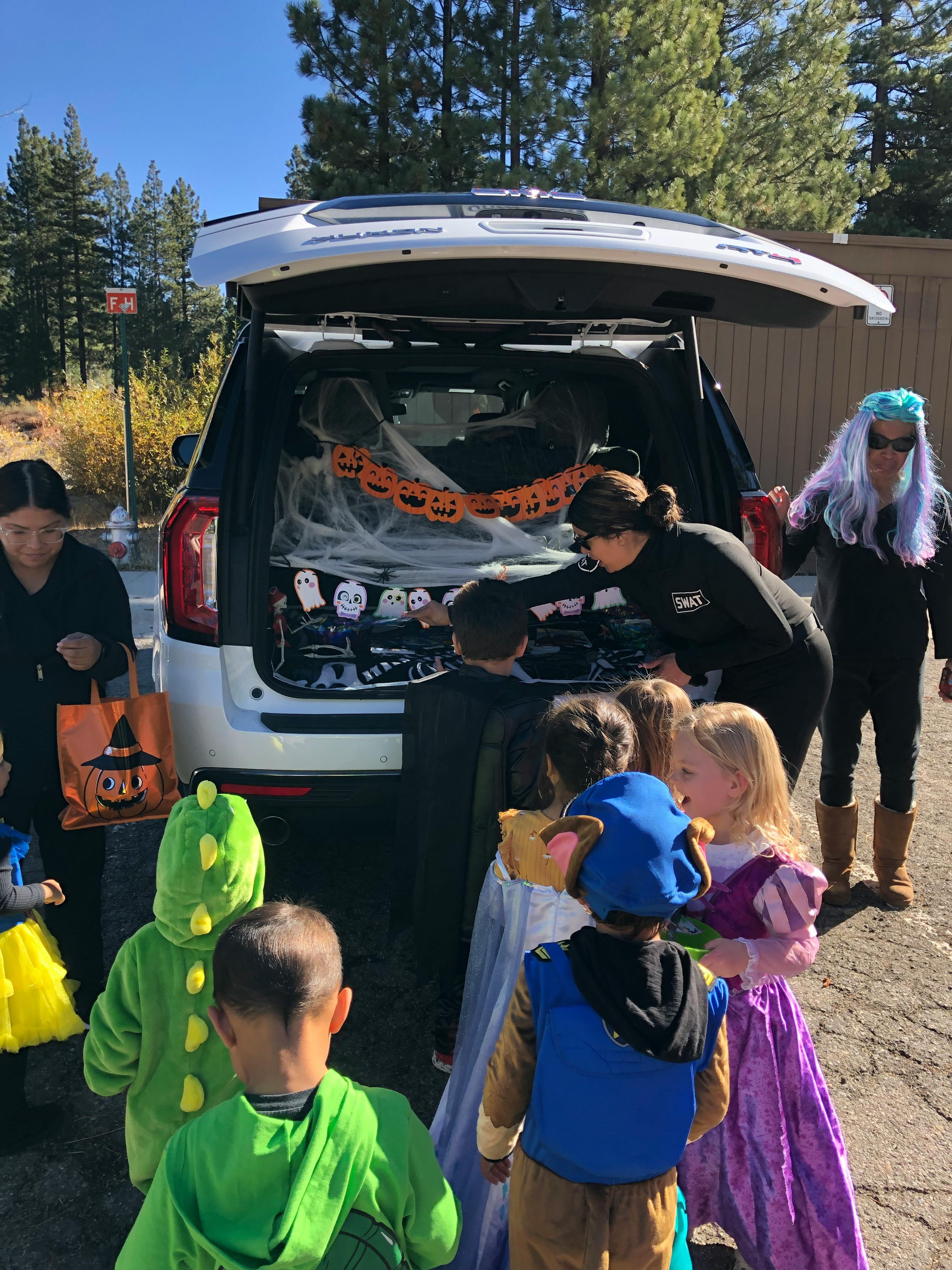 People and children in costumes around a decorated car trunk