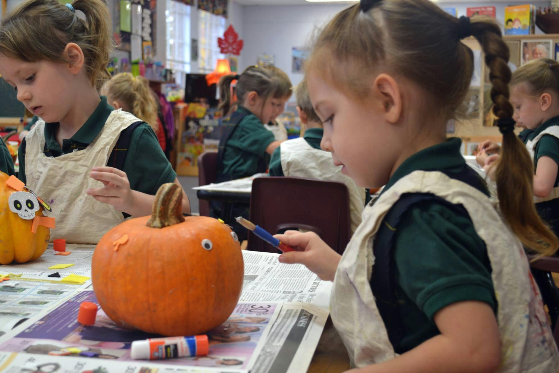 Child decorating a pumpkin at a table with other children