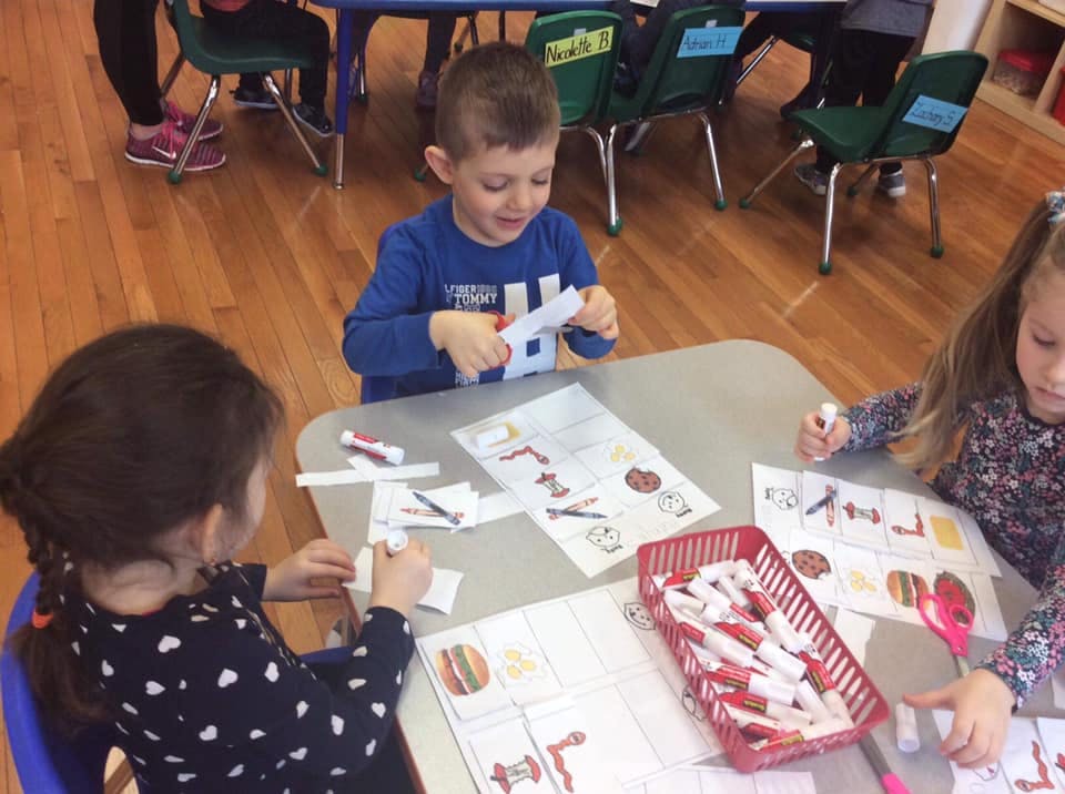 Three children cutting and coloring at a table