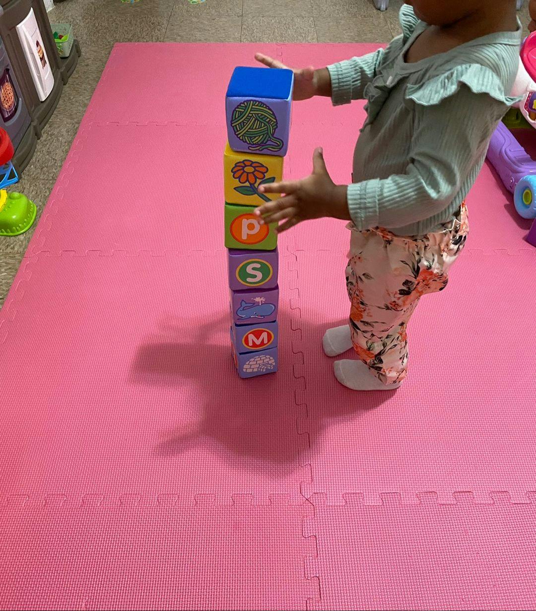 Child standing next to a tall stack of colorful alphabet blocks
