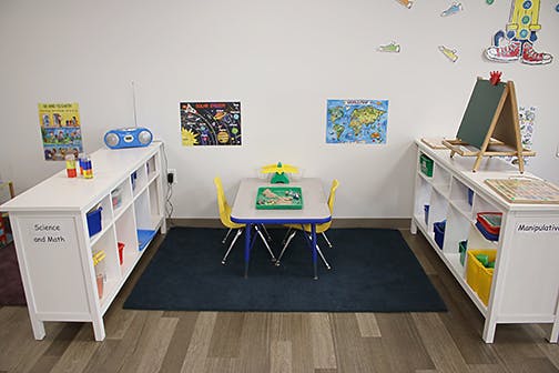 Children's classroom with small table and chairs, shelves, and an easel
