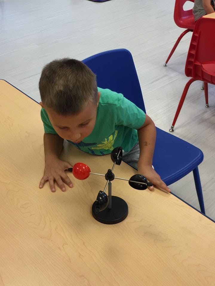 Child looking at a small weather vane on a table