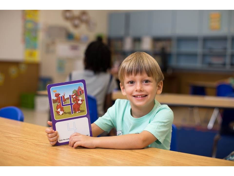 Child holding up a learning card with the number 4 in a classroom