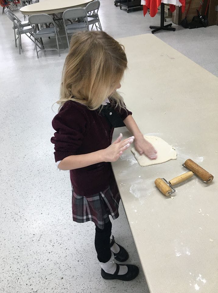 Child pressing dough on a counter with two small rolling pins nearby