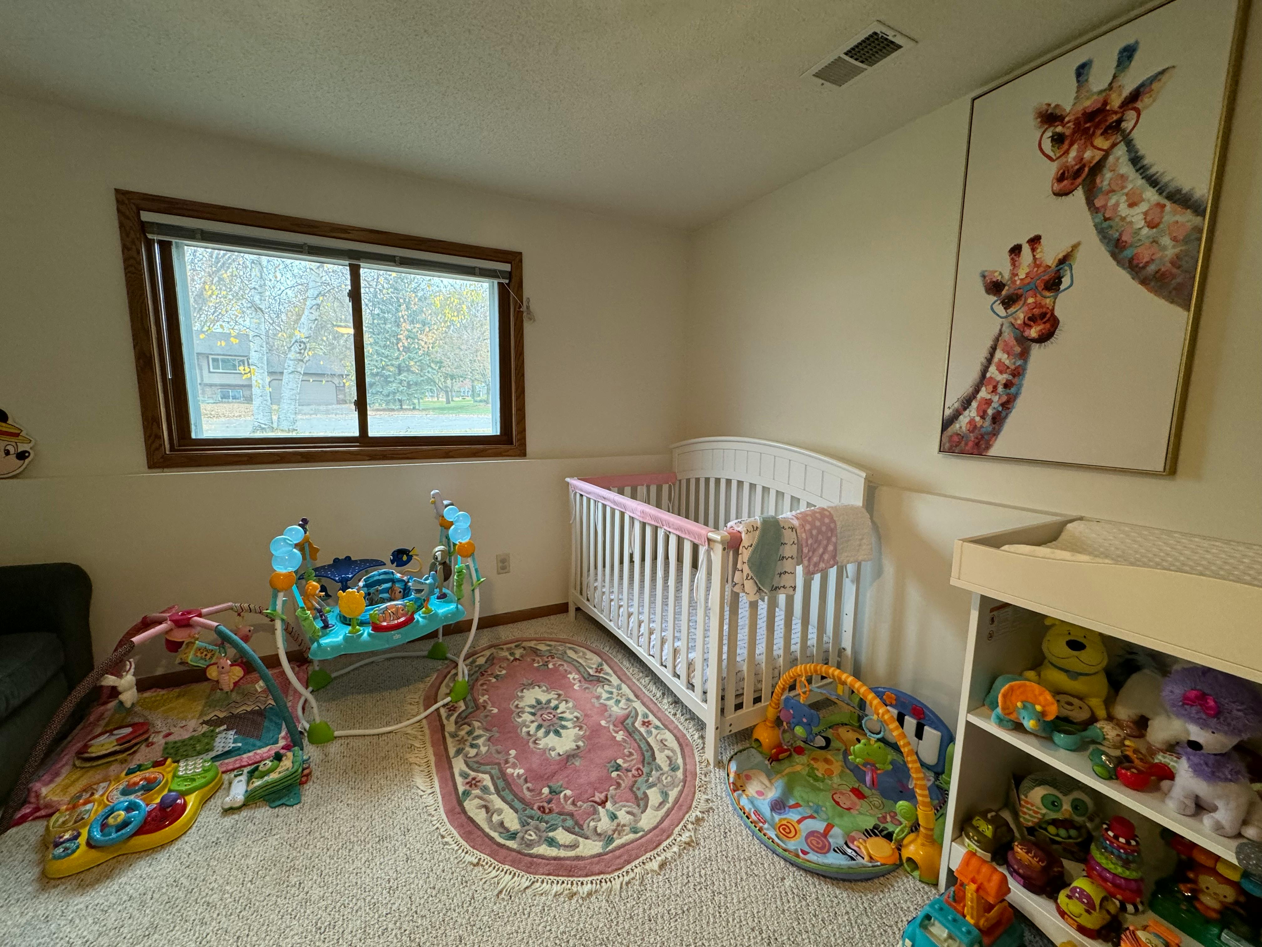 Baby nursery with a white crib, play mats, and a giraffe painting