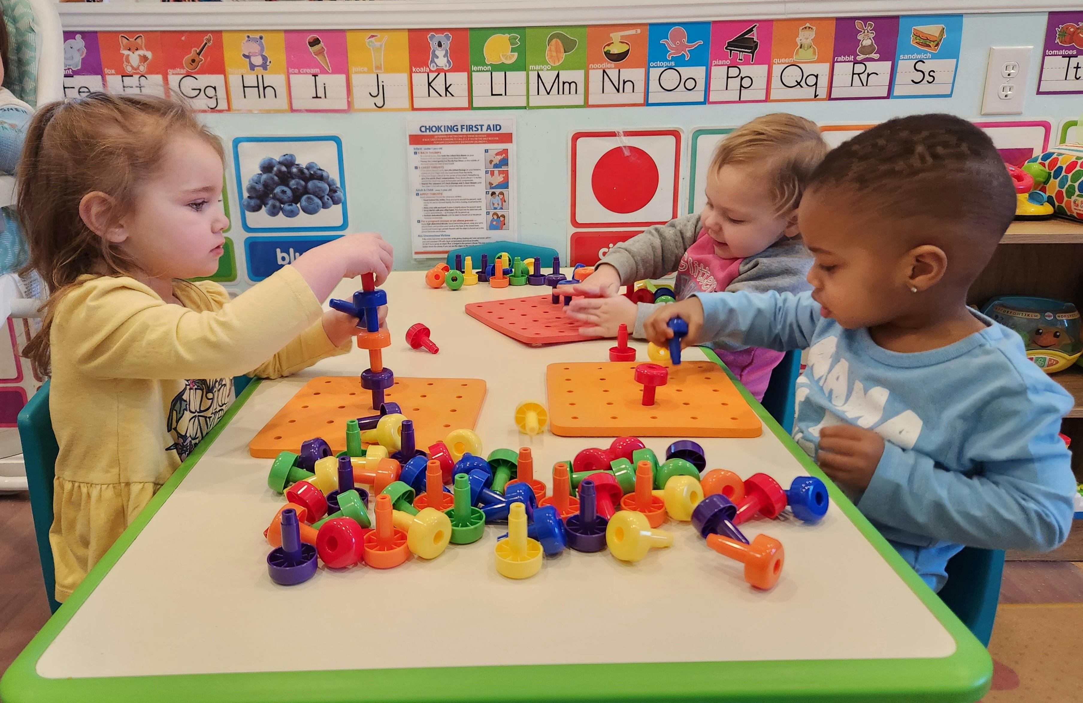 Three children playing with colorful pegboards and pegs at a table