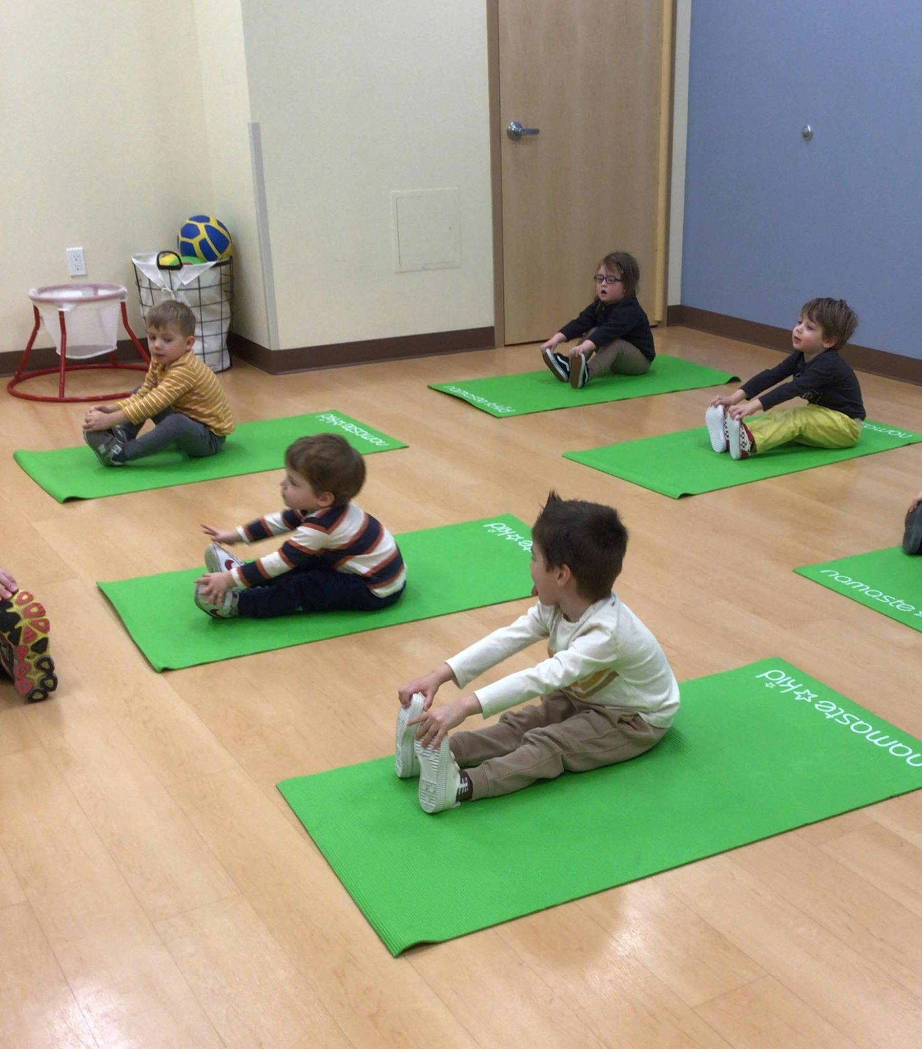 Children sitting on green mats stretching