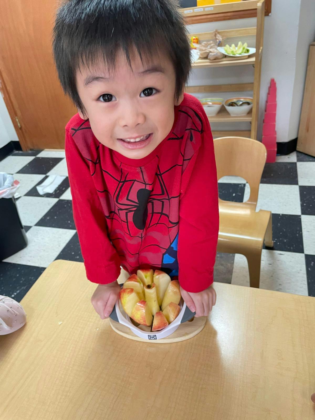 Child in red shirt with apple slices on a table