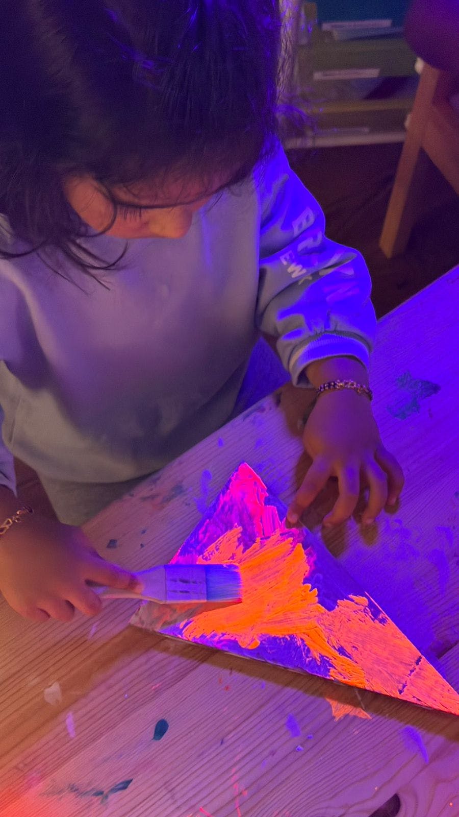 Child painting a triangular shape with a glowing orange color