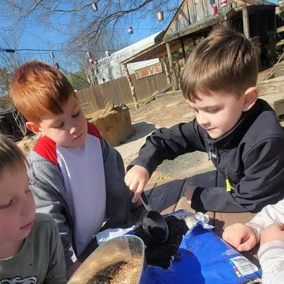 Children scooping dirt on a table outdoors