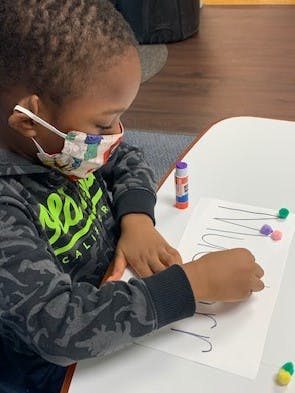 Child in a mask working on a craft at a table