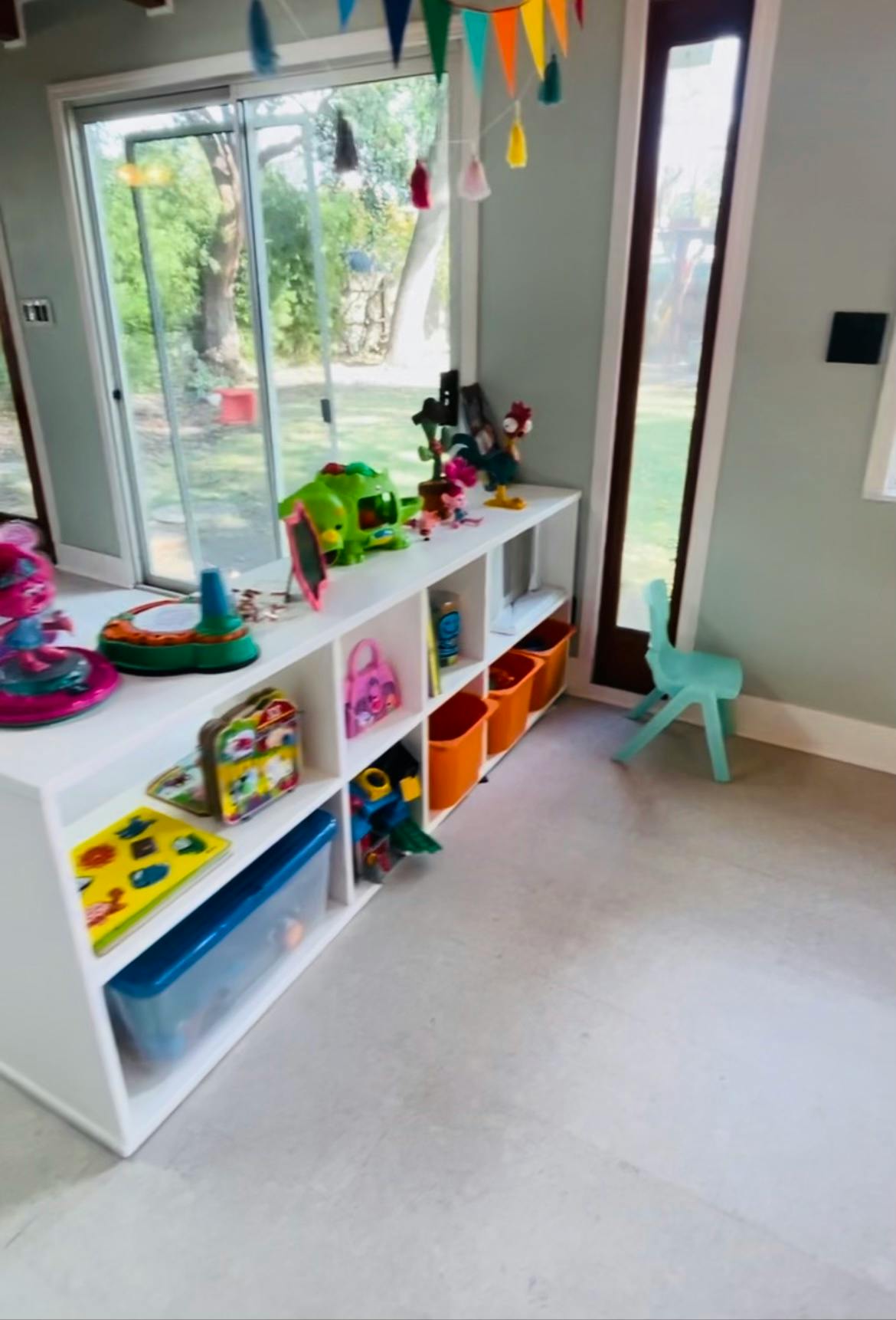 White shelving unit filled with toys and storage bins in a room with a large window