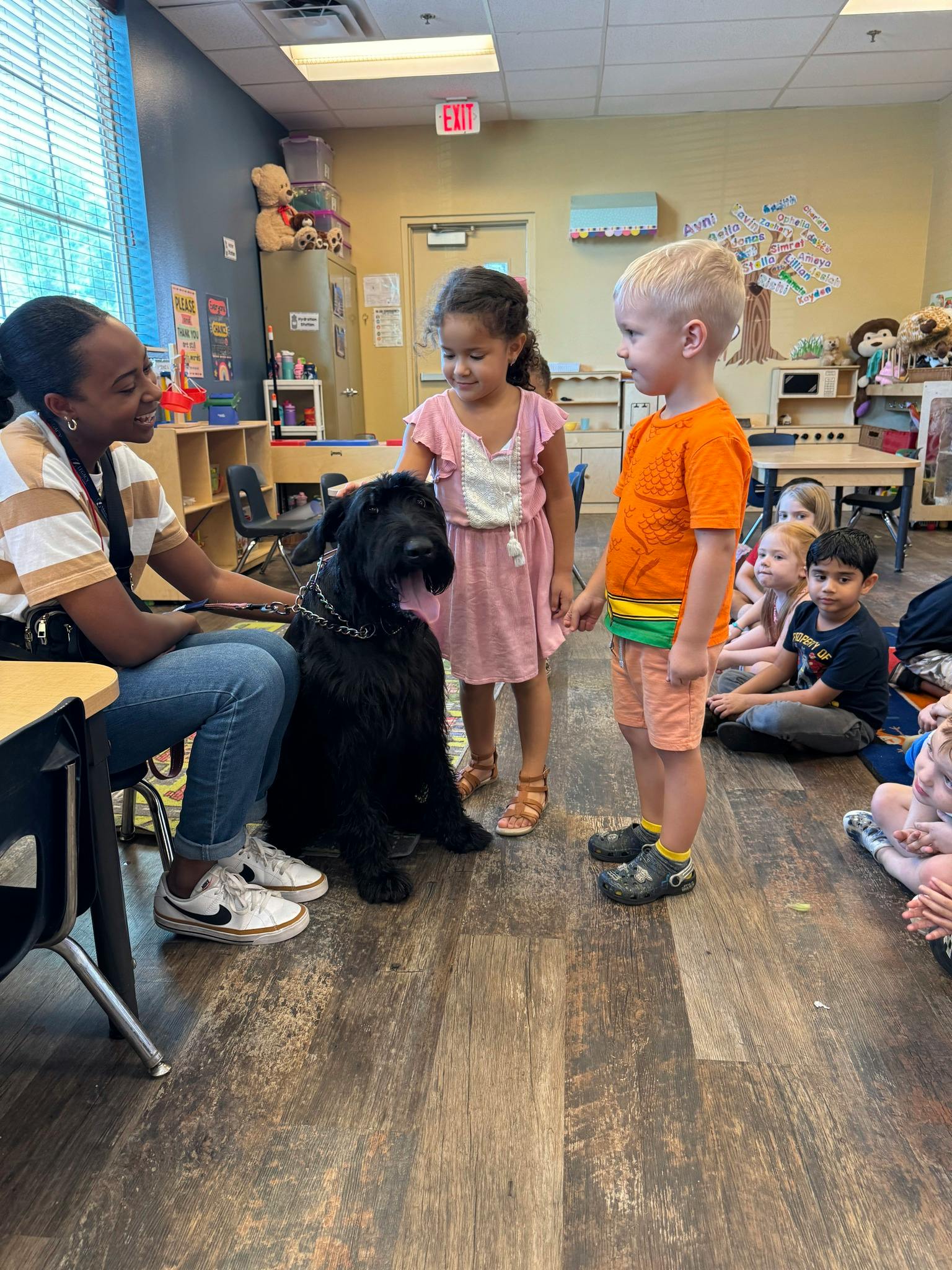 Person with a large black dog and two children in a classroom