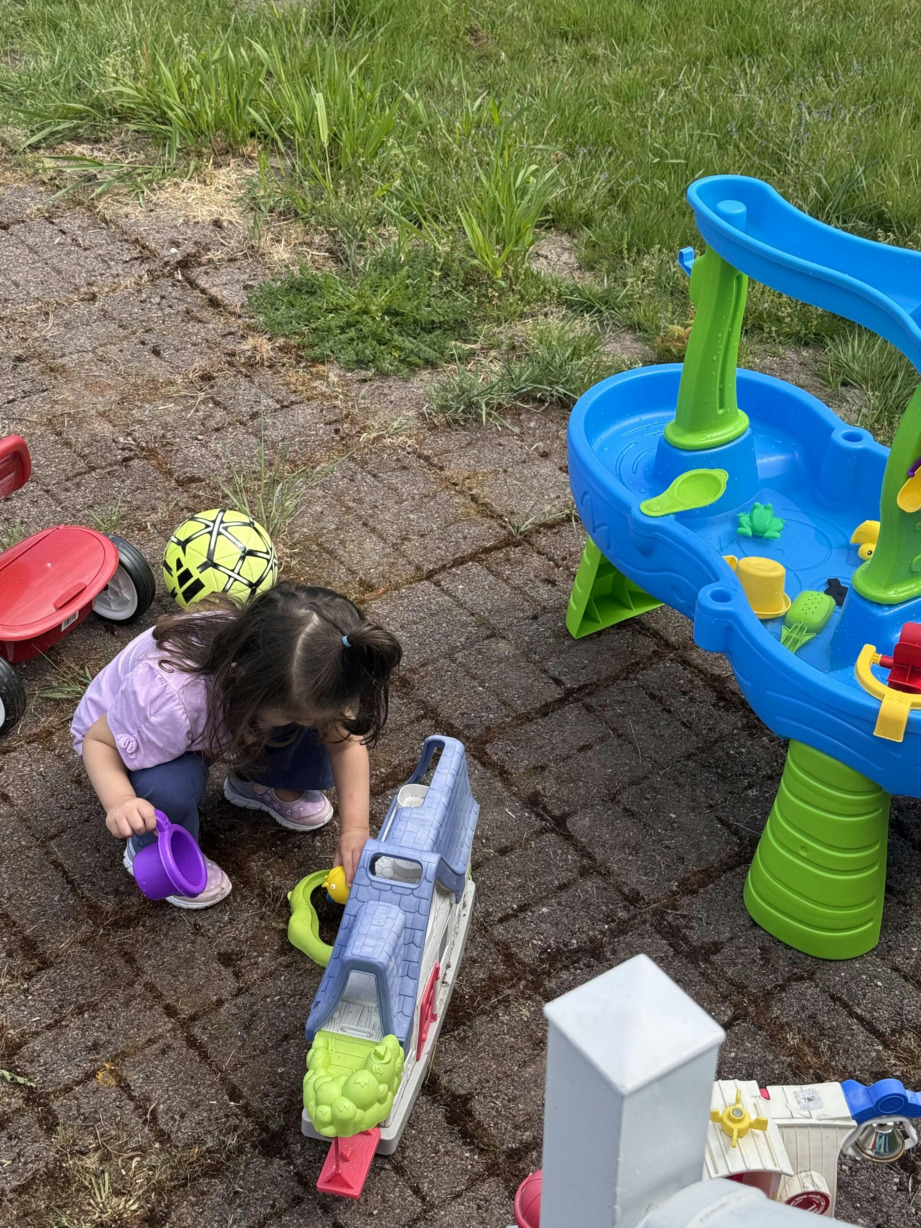 Child crouching and playing with outdoor toys on a paved surface