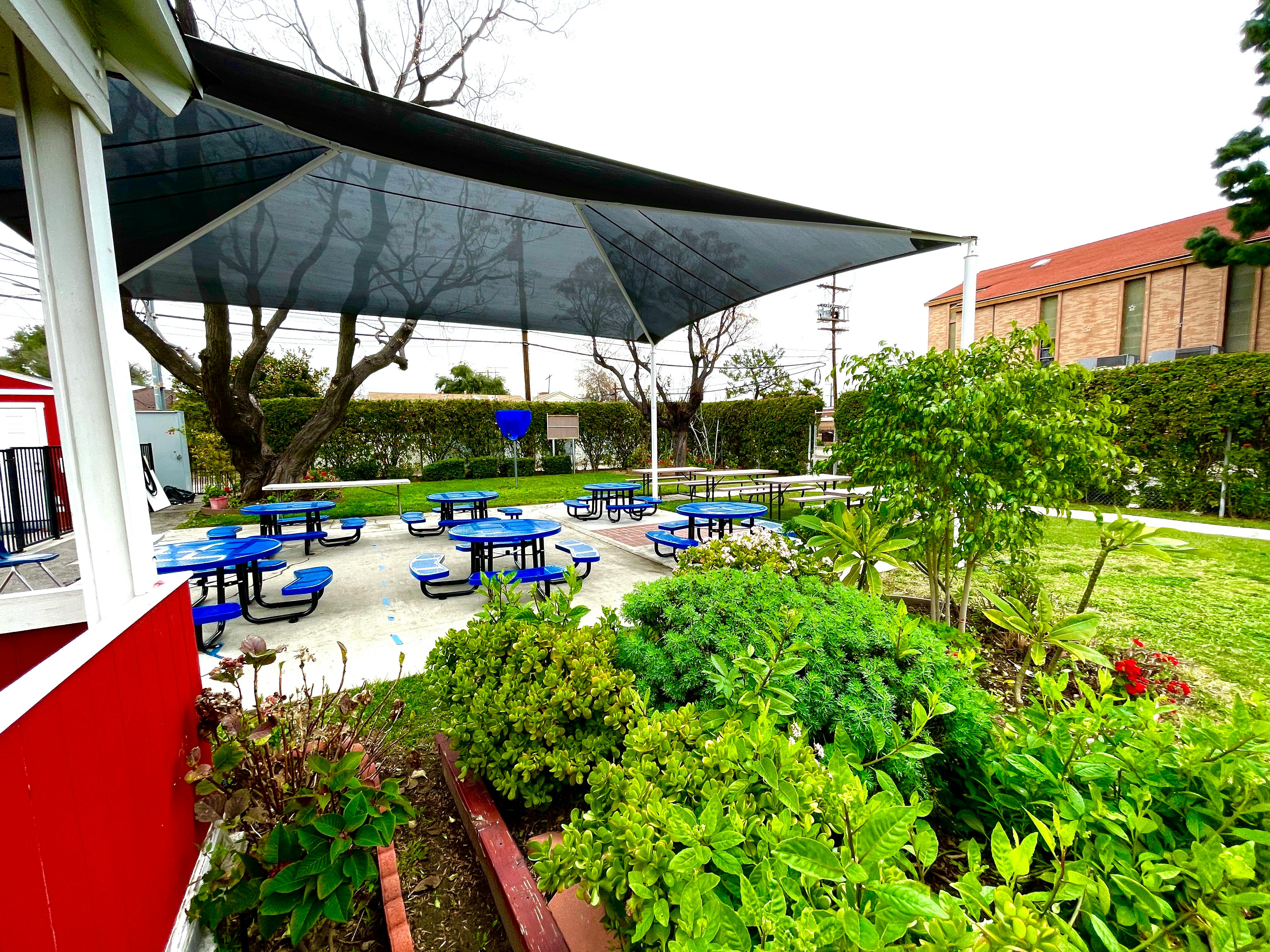 Outdoor patio with blue picnic tables under a large shade canopy