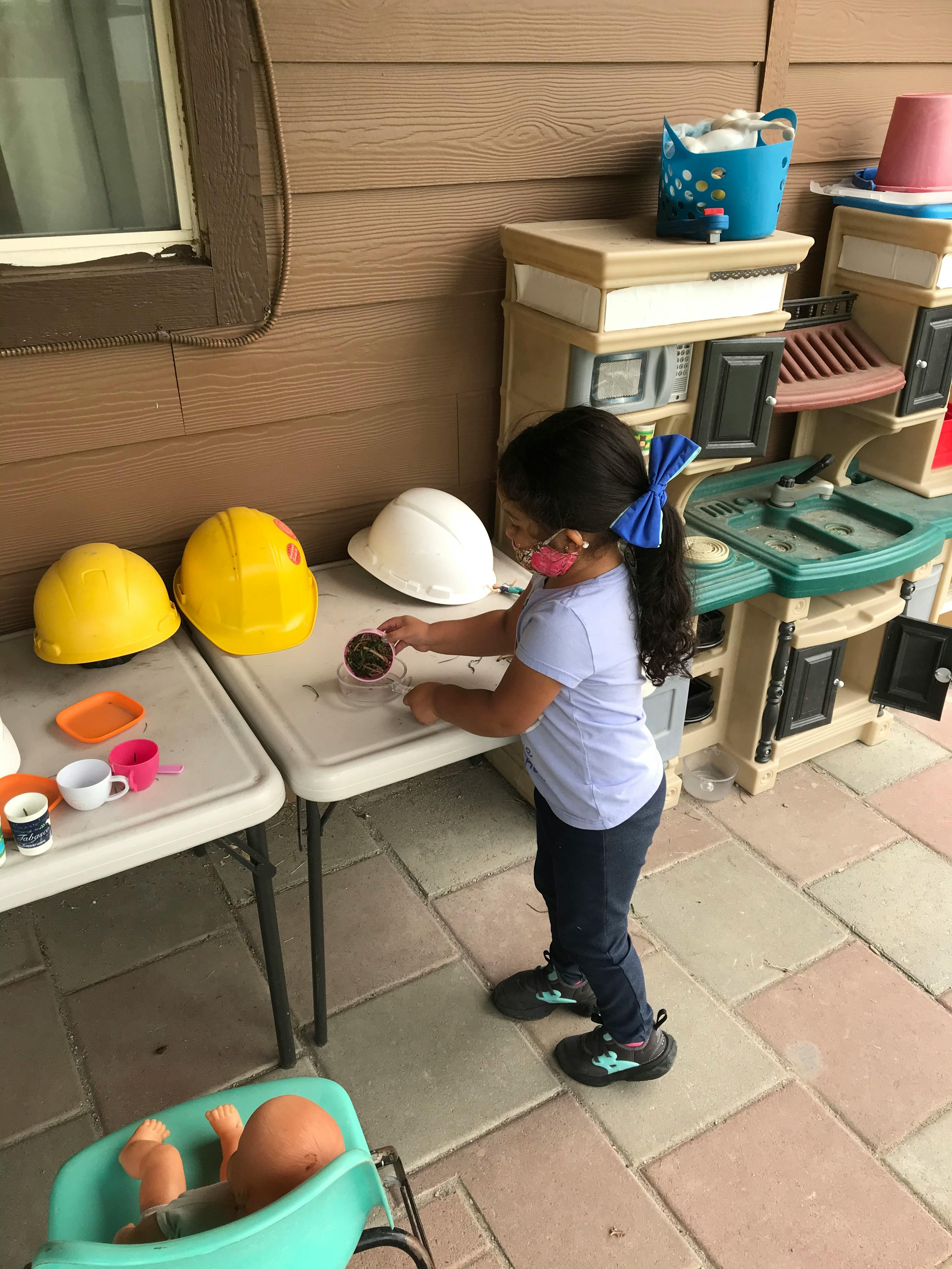 Child playing with toy cups and hard hats on a patio