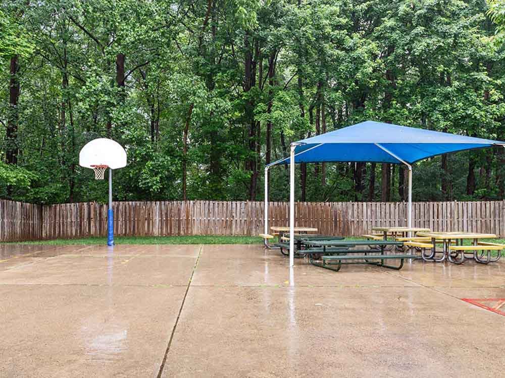 Wet outdoor court with a basketball hoop, covered tables, and a wooden fence