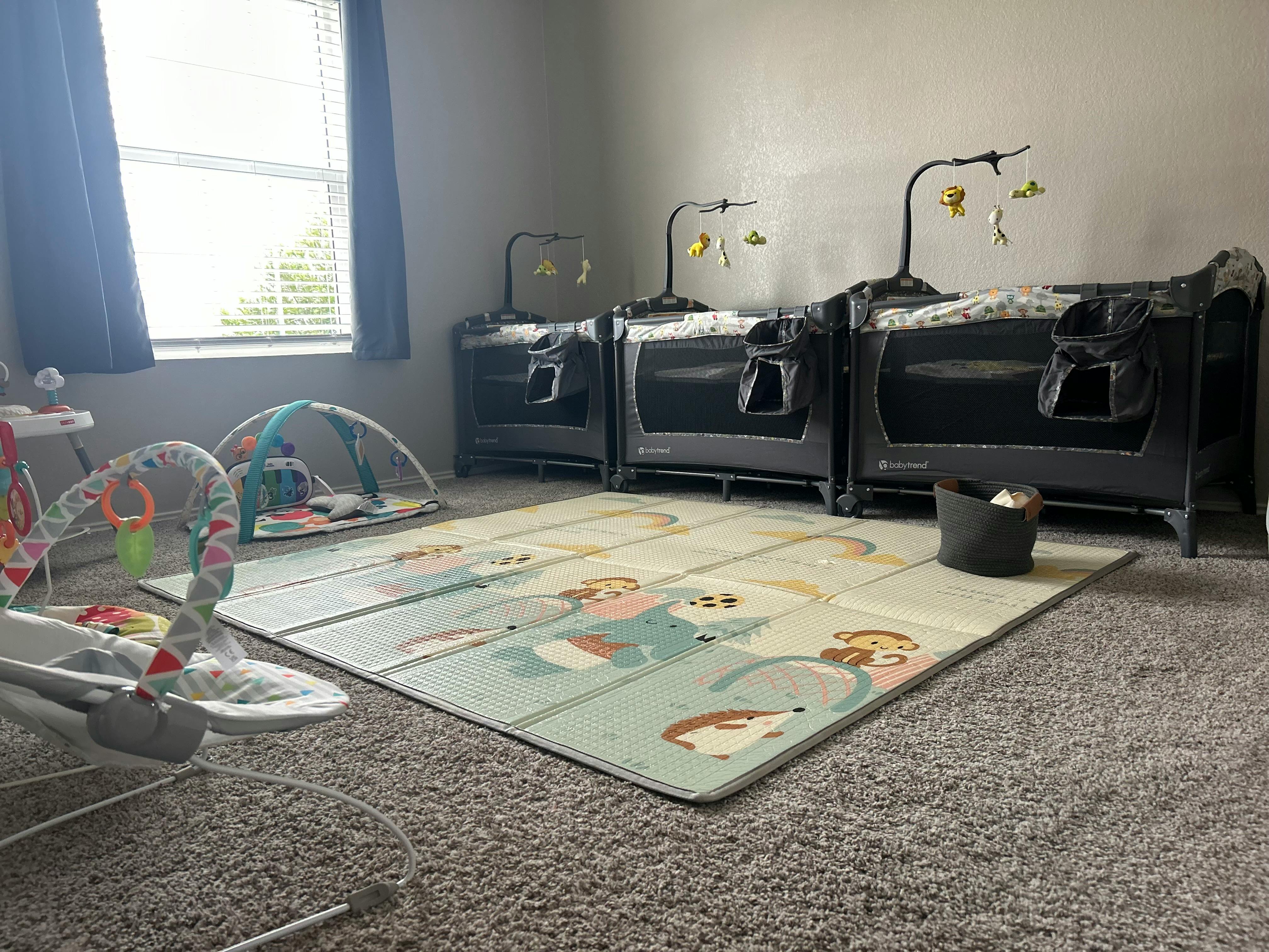 Three baby cribs lined up against a wall with a playmat on the floor