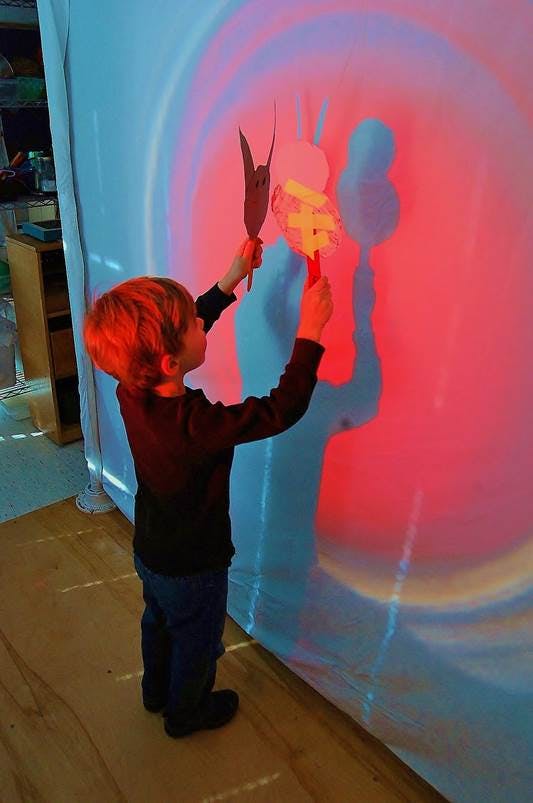 Child holding up paper cutouts against a colorful light projection on a wall