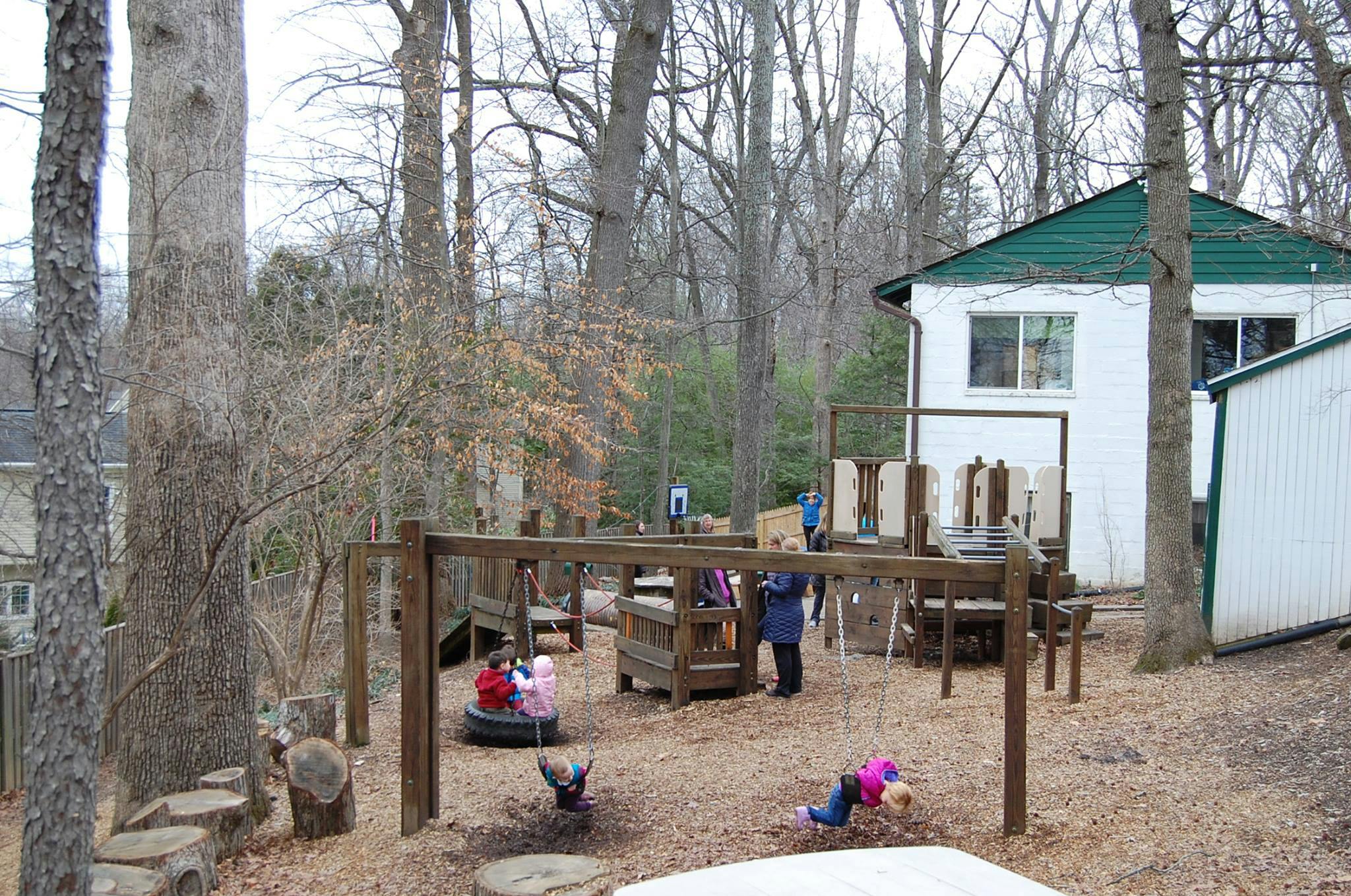 Children playing on a wooden playground structure in a wooded area
