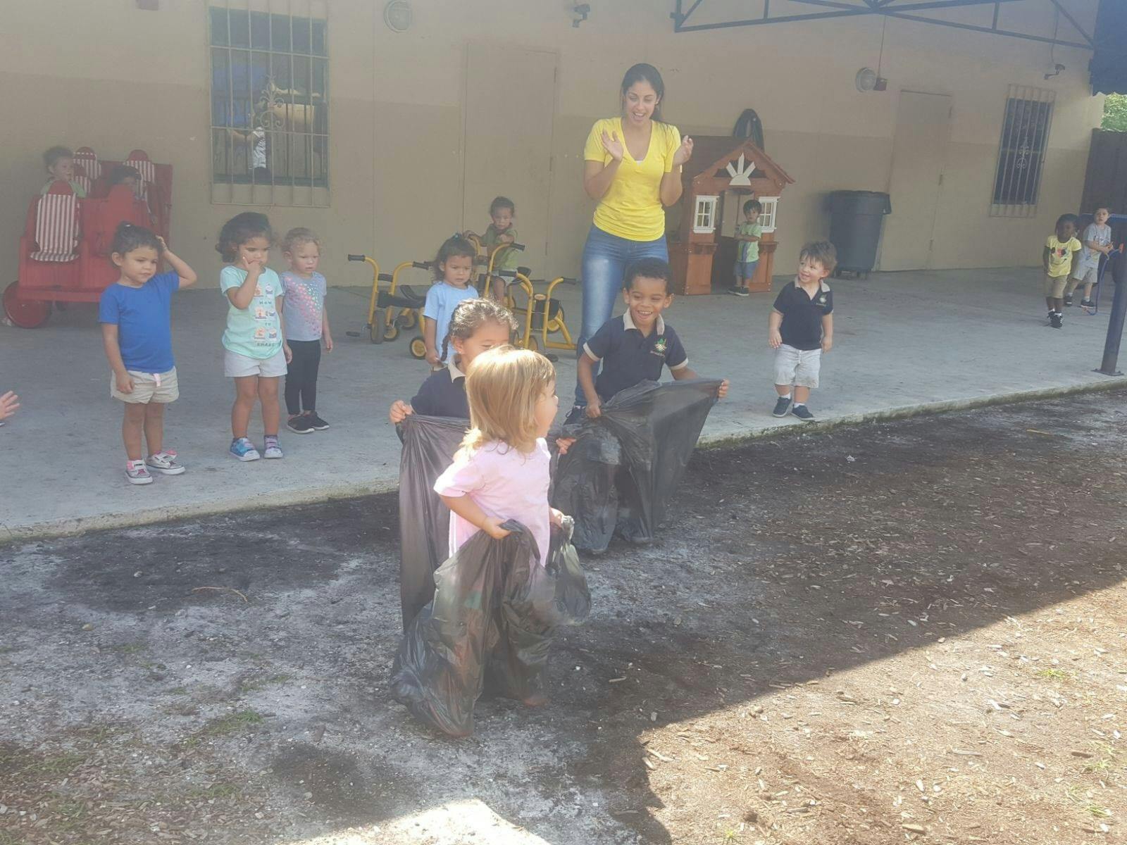 Children participating in a sack race outdoors with an adult supervising