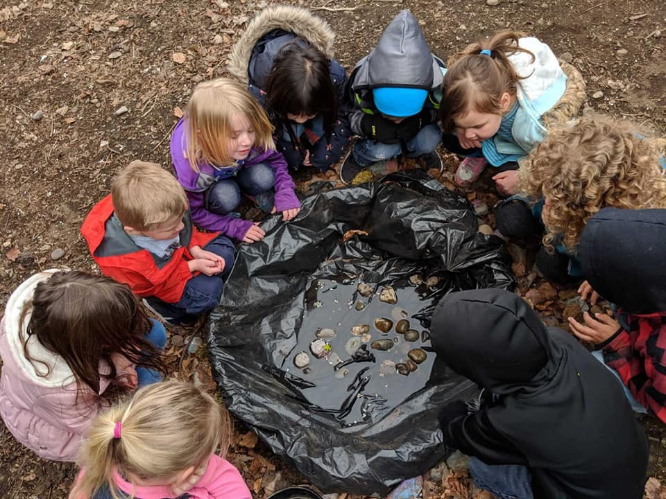 Children gathered around a black tarp with objects inside