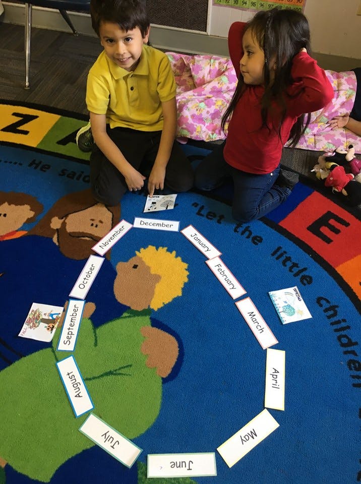 Two children sitting on a rug with month cards arranged in a circle