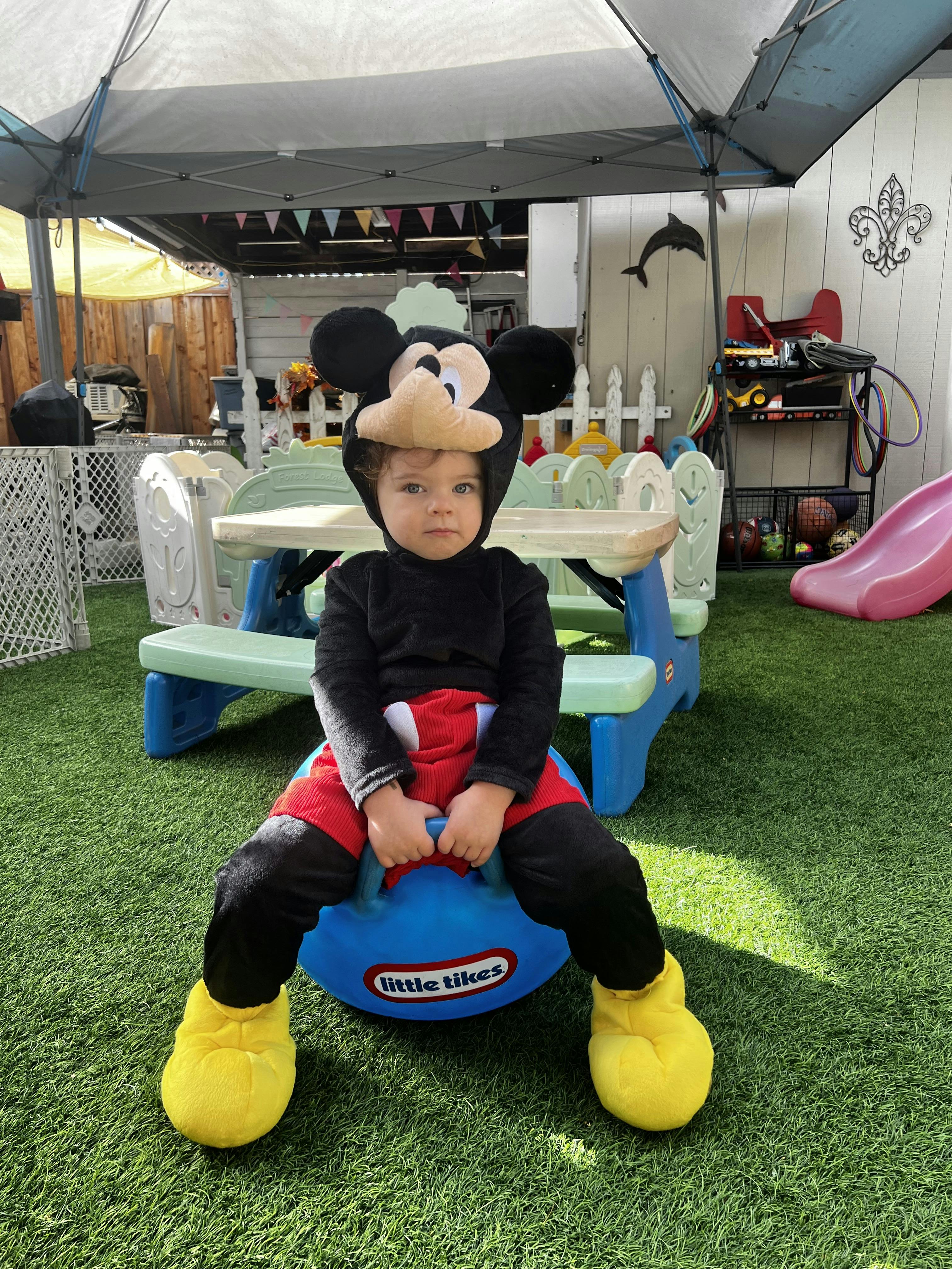 Child in Mickey Mouse costume sitting on a blue Little Tikes toy