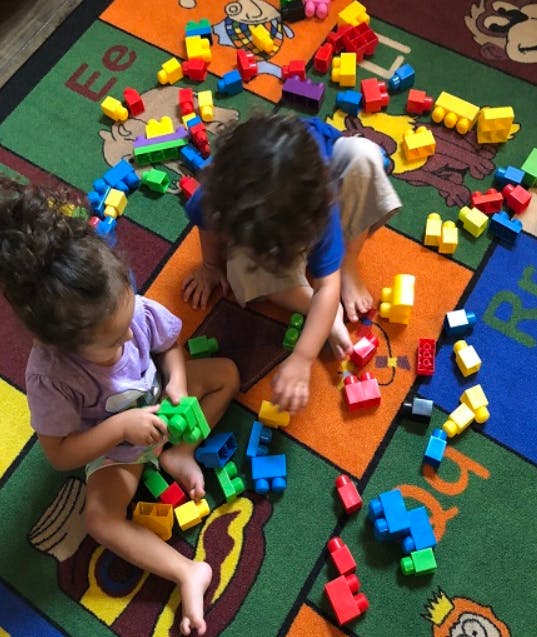 Two children playing with colorful building blocks on a patterned rug