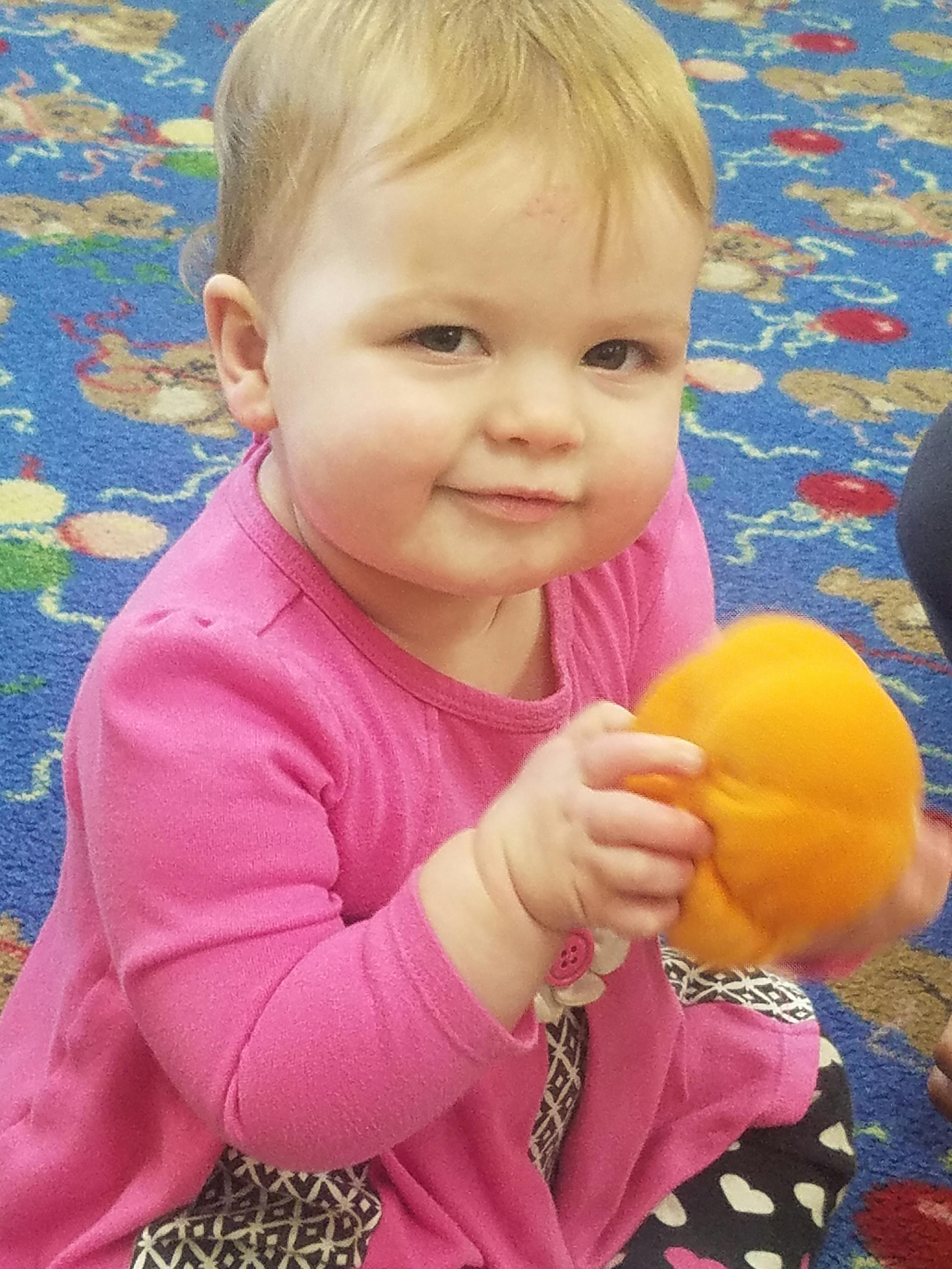 Child in pink shirt holding an orange toy