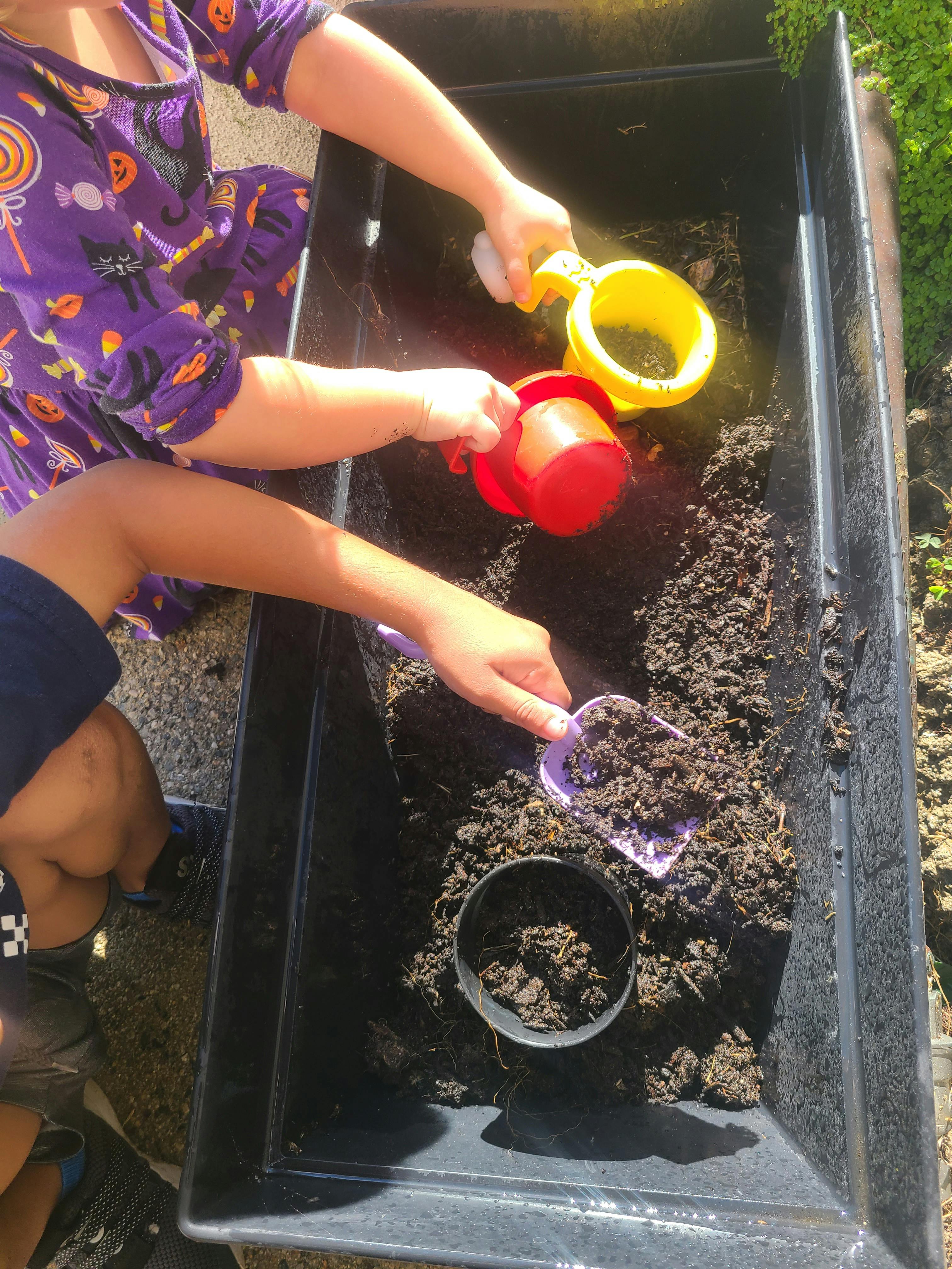 Child playing with dirt and scoops in a black bin