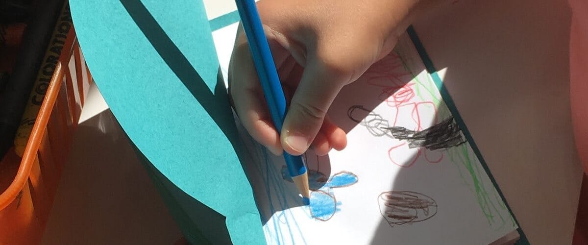 Child's hand coloring with a blue pencil on paper