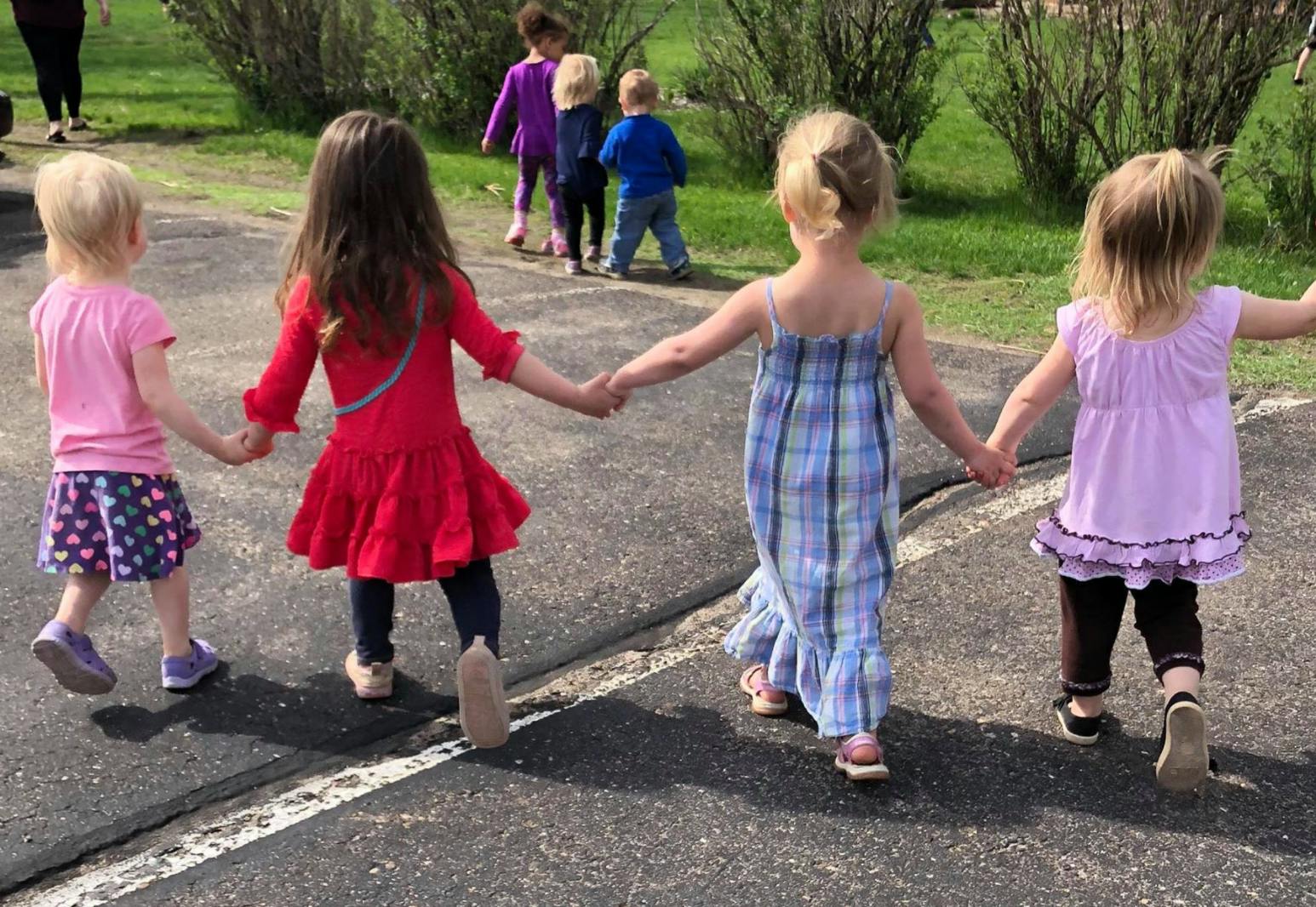Four children holding hands and walking away from the camera