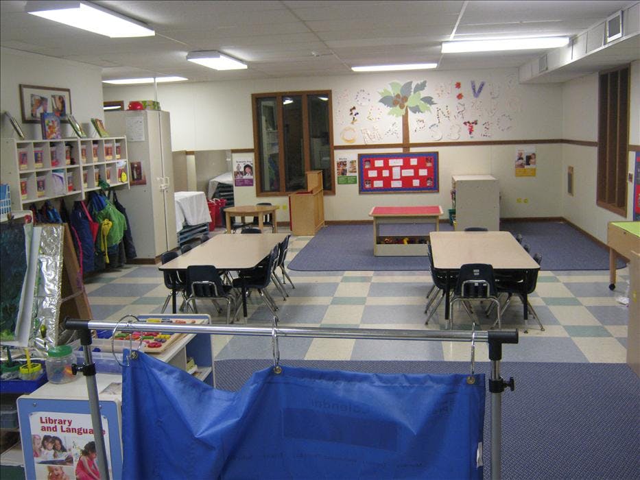 Classroom with small tables and chairs, coats hanging on a rack