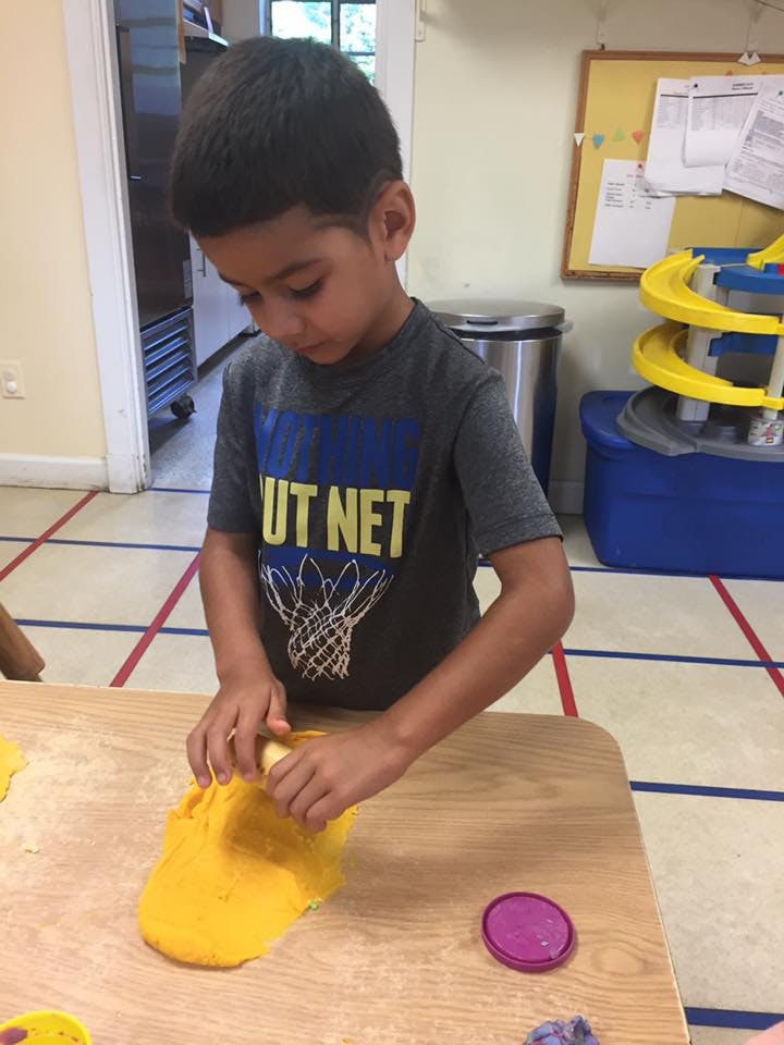 Child playing with yellow playdough at a table