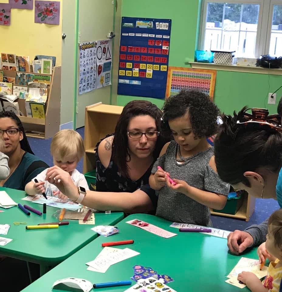 People and children drawing and coloring at green tables in a classroom