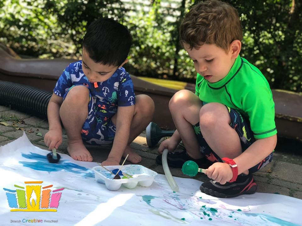 Two children painting on a large white sheet outdoors