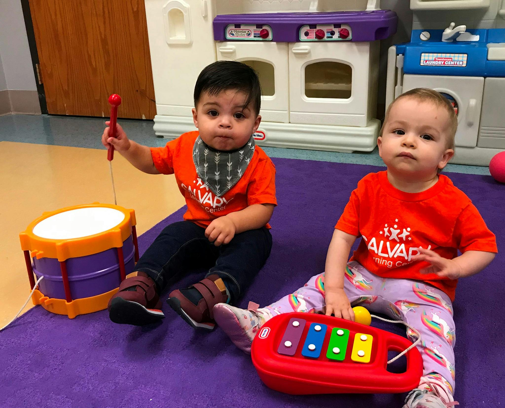 Two children sitting on a mat with musical toys