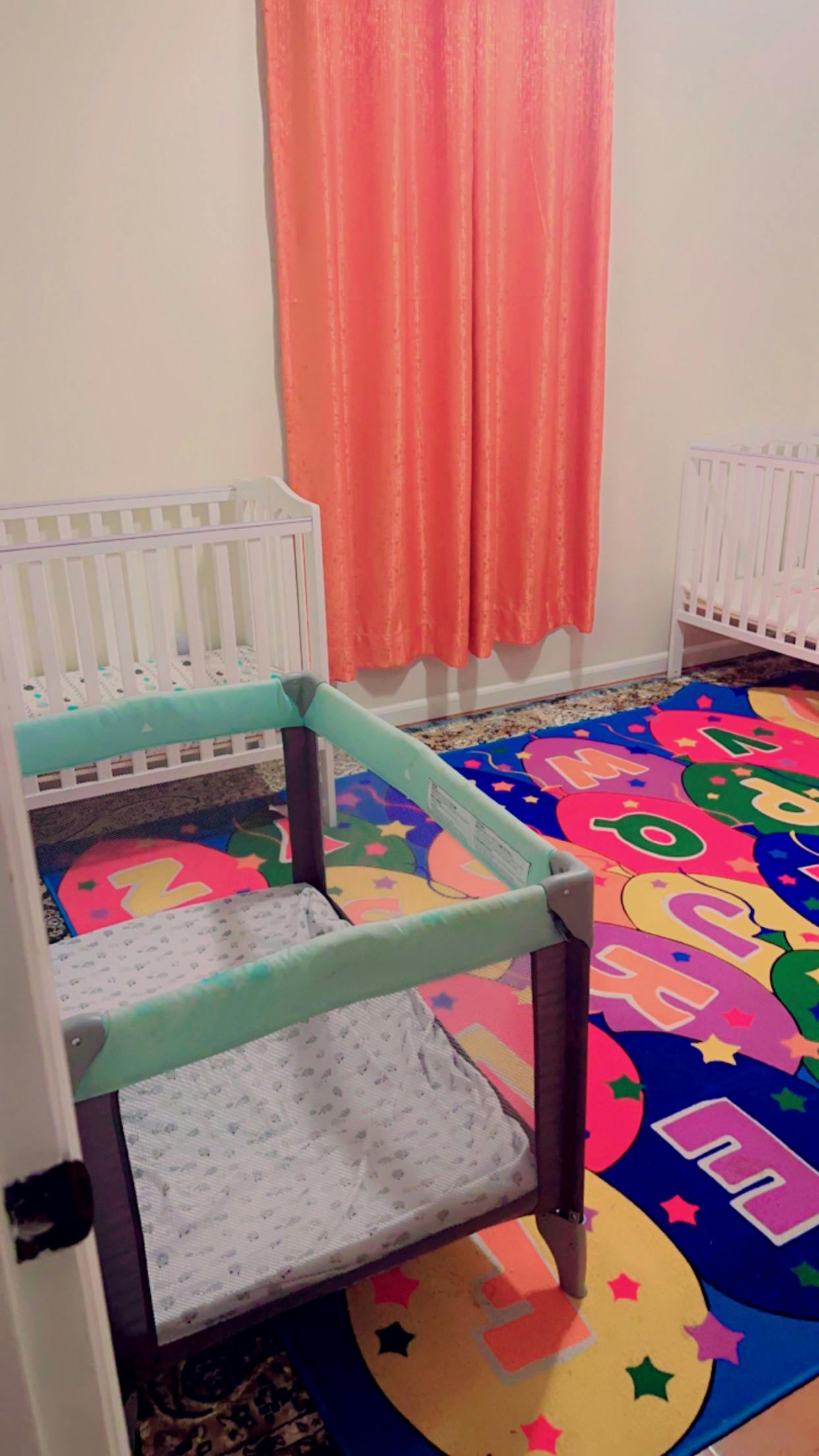 Two cribs and a playpen in a room with a colorful alphabet rug