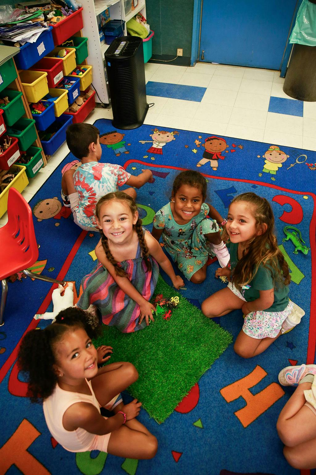 Four children playing on a blue rug with a green mat in a classroom