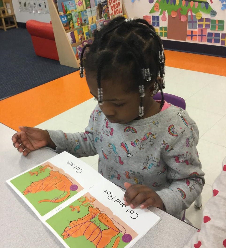 Child looking down at a book with illustrations of a cat and rat
