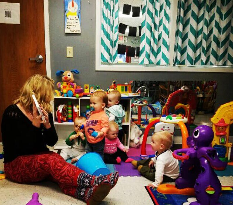 Person on phone with multiple children playing in a room