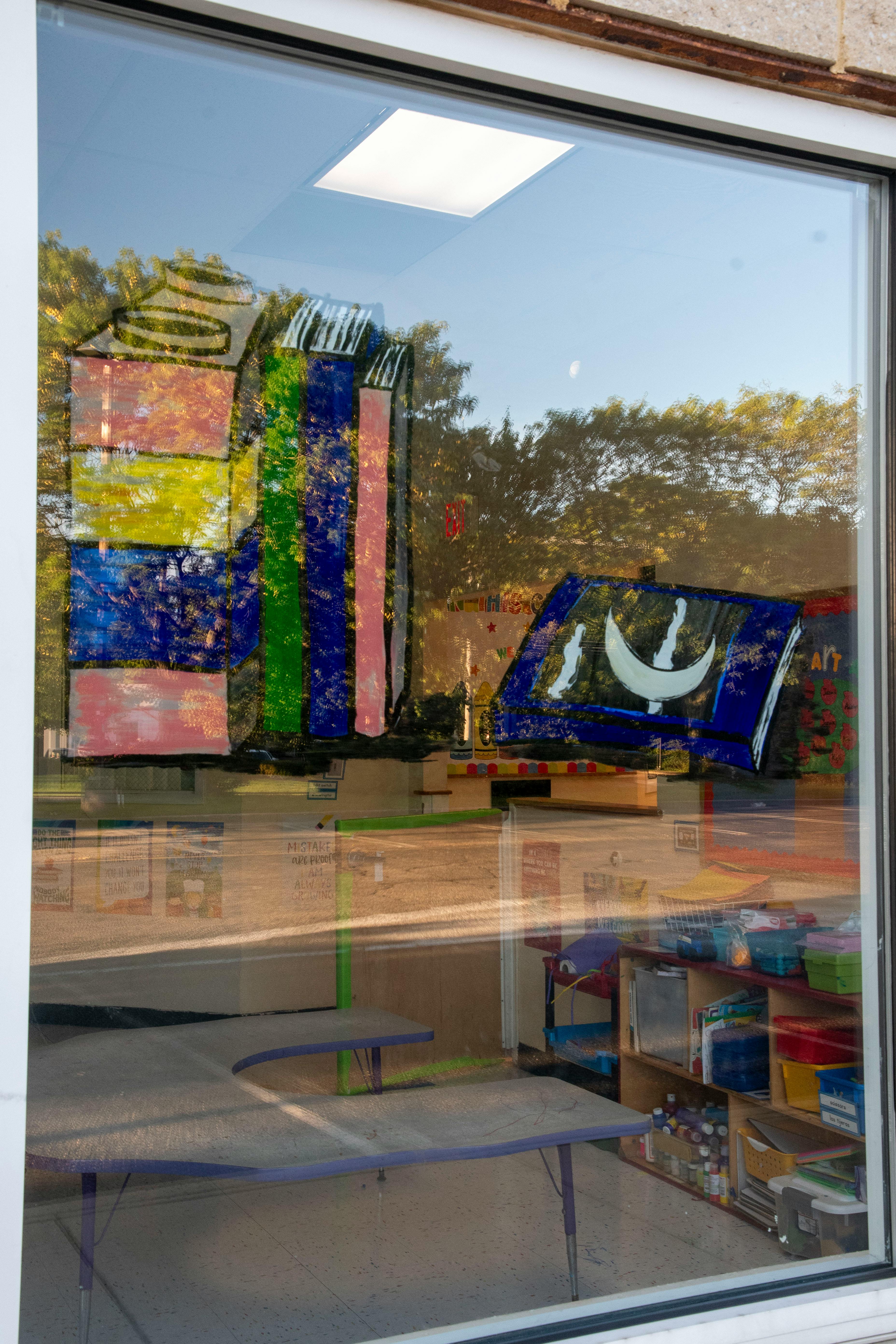 Window with colorful painted decorations and reflections of trees