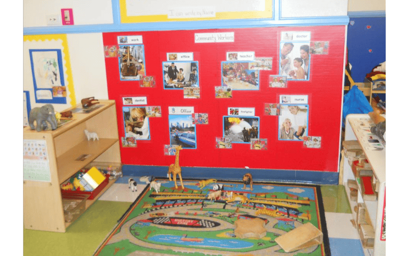 Classroom with a red bulletin board about community workers and a rug with toy animals