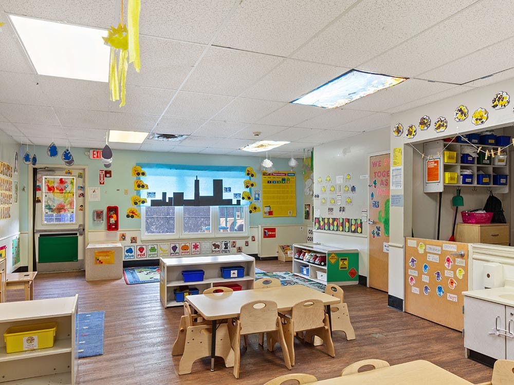 Empty classroom with small tables and chairs, decorated walls and windows