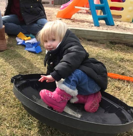 Child in a black coat and pink boots sitting in a black sled