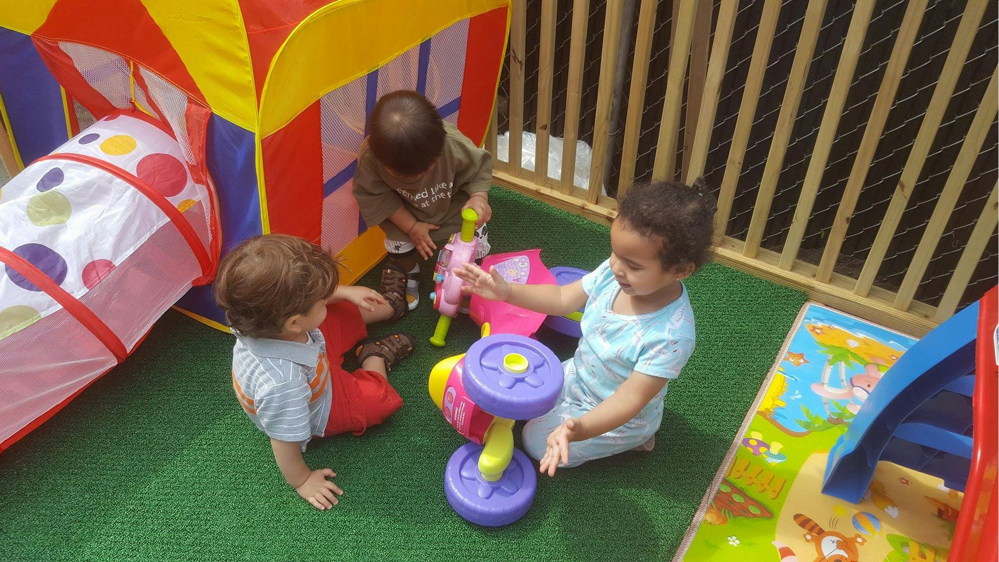 Three children playing with toys on a green mat